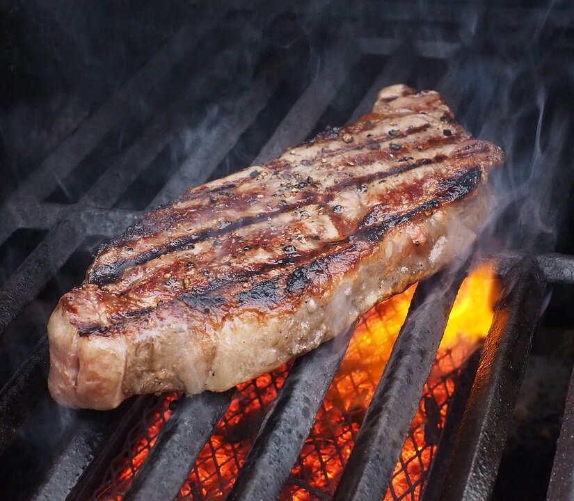 Grilled steak cooking on a barbecue grill, showcasing a perfectly seared crust with grill marks and smoke rising, highlighting the juicy texture and rich flavors of the meat.